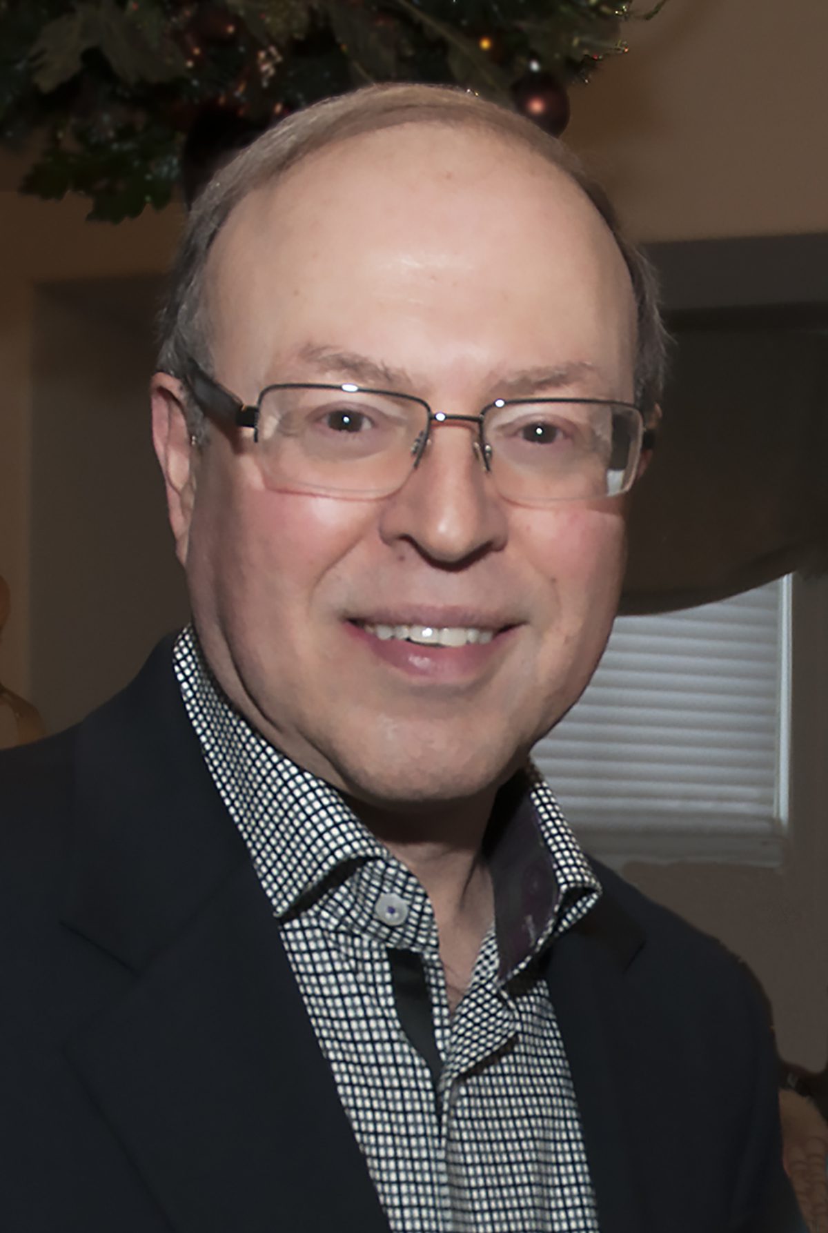 A smiling man wearing glasses and a suit jacket indoors.